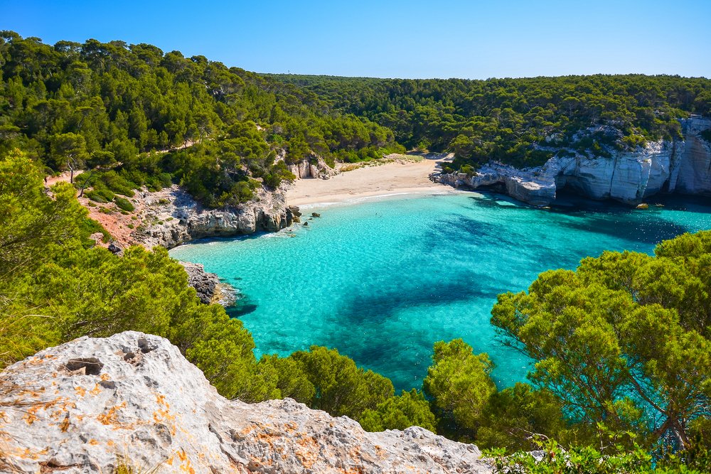 Aqua blue sea cove and beach in Menorca, visited using car hire by easyCar